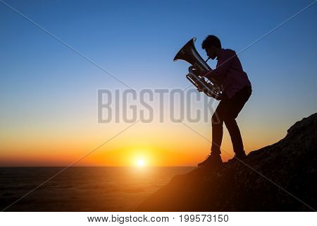 Musician silhouette play Tuba on sea shore at sunset.