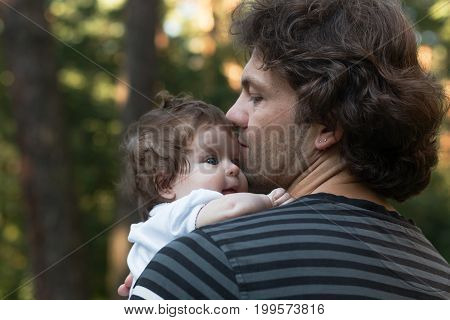 Dad holding his little blue-eyed daughter in his arms for a walk in the park. Summer day, family nature walk, sunny.