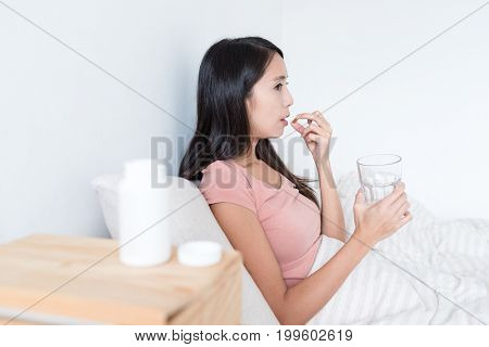 Woman taking medicine and holding glass of water on bed