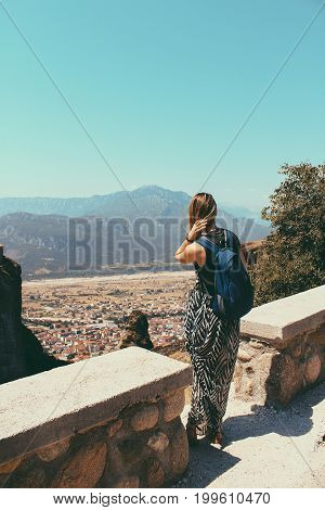 A Young Tourist Woman With A Backpack Stands On A High Mountain Point, Enjoying Beautiful View Of Gr