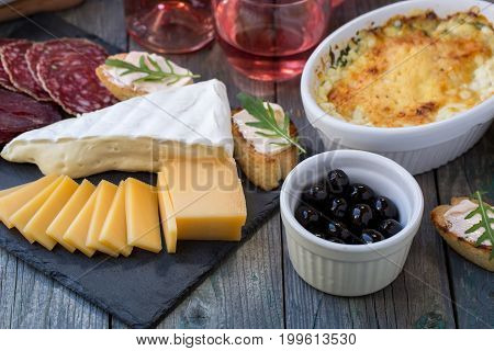 Board with basturma, salami, camembert, cheese, other delicacies and pink wine.