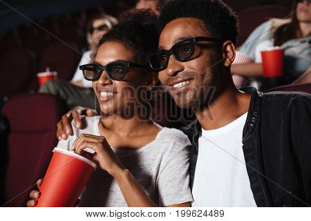Smiling attractive afro american couple watching 3D movie and eating popcorn while sitting in a movie theater