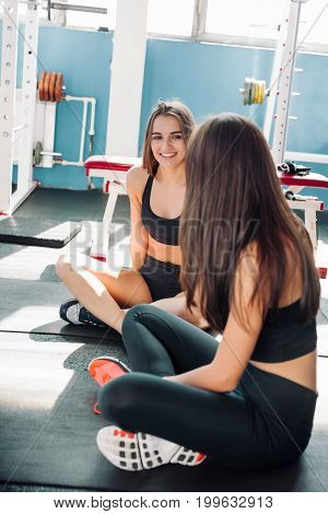 fitness sport training gym and lifestyle concept - two smiling women sitting on the half ball and relaxing after class in the gym