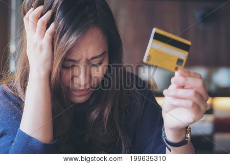 Close up image of an Asian woman close her eyes while holding credit card with feeling stressed and broke