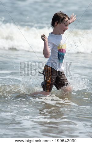 View of A happy young boy child running playing and having fun in the surf and waves of a sandy sunny beach