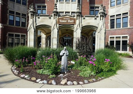 JOLIET, ILLINOIS / UNITED STATES - JULY 17, 2017: A sculpture of Saint Francis stands in a flower garden in front of Tower Hall at the University of Saint Francis.