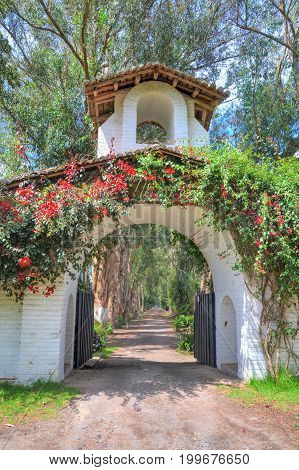 Entrance to an old hacienda converted to a public  restaurant, with a tower, gate, flowers and an old dirt road, Pichincha Province, Ecuador.