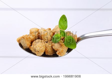 spoon of soy meat cubes on white wooden background