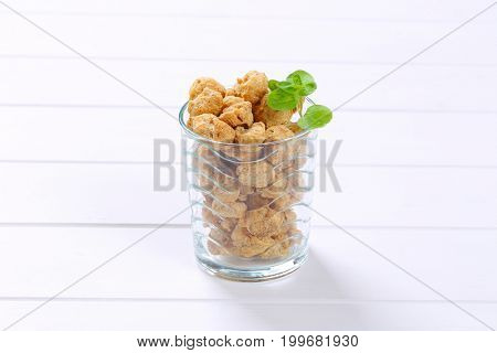 glass of soy meat cubes on white wooden background