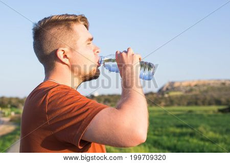 Closeup portrait of young guy drinking water from bottle on a hot sunny day.