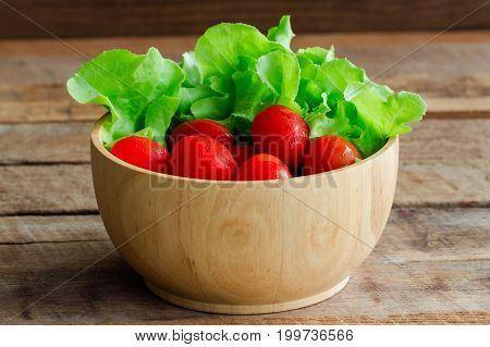 Fresh tomato and lettuce in wood bowl put on wood table. Side view close up of tomato and green oak lettuce with copy space for background. Fresh green oak lettuce and tomato prepare for cooking. Green lettuce and red tomato concept.