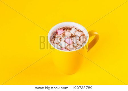 Yellow cup of hot cocoa with marshmallows on yellow background