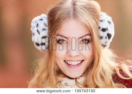 Portrait of pretty smiling fashionable woman in fall forest park. Happy gorgeous young girl in fur earmuffs. Autumn winter fashion.