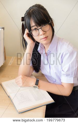 Cute Asian Thai high school girl in uniform with glasses is looking up while study in her room in schoolgirl fashion and education concept.