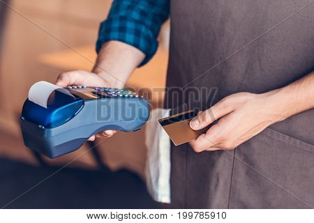 partial view of barista holding credit card and cardkey reader in hands in cafe