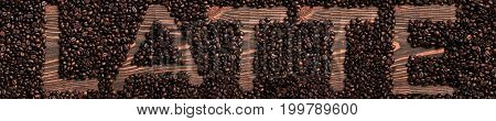 Latte word written with wooden letters on coffee beans heap. Top view