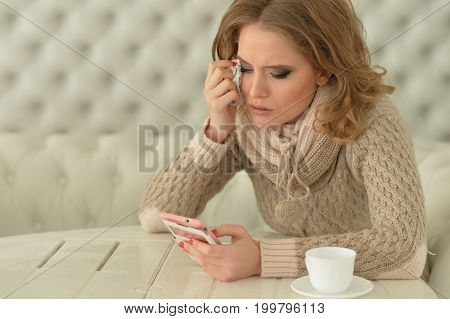 Portrait of a young beautiful crying woman using smartphone
