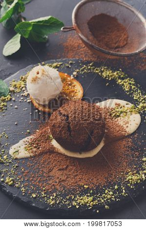 Exquisite french dessert. Chocolate fondant with creme anglaise and vanilla ice cream, sprinkled with cocoa, served on round slate finely decorated with orange citron and pistachio crumble, closeup