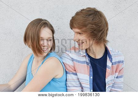 Couple Of Teenagers Being In Love, Having Fun While Sitting Next To Each Other, Looking With Love. L