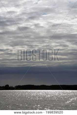 Sunlight on the surface of the lake. Glare the sky clouds. contrast water and light