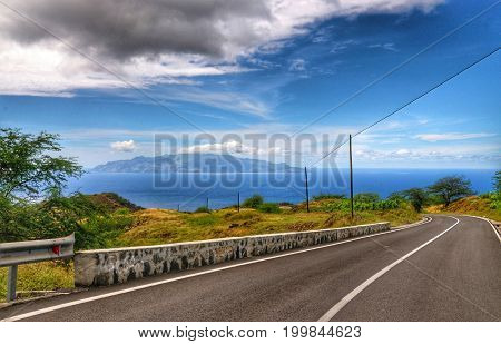 Newly asphalt road on the island of Fogo descends towards the capital city with sister island of Brava in view at sea.