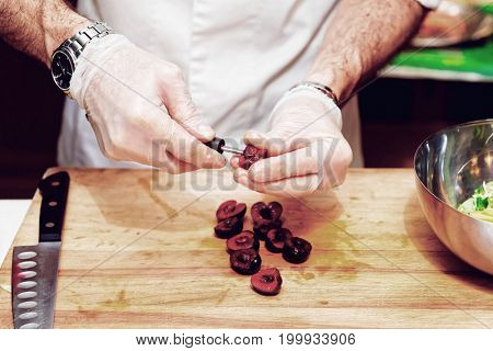 Chef is removing stones from cherry in professional kitchen, toned image