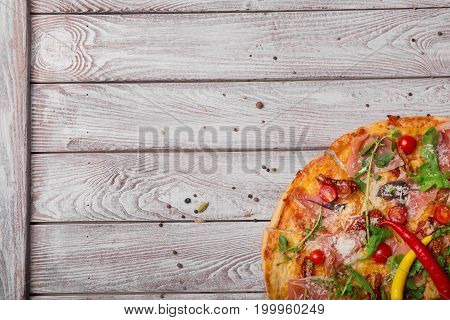 A close-up picture of a tasty apicollo pizza with bright hot chili peppers and italian spicy meat.Tasty dish on a rustic wooden table background. Cooking, baking concept. Copy space.