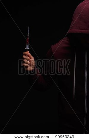 Addict male with a syringe full of drugs on a saturated black background. A hopeless drug addict is going through addiction crisis. Fear, depression, abuse, addiction concept.