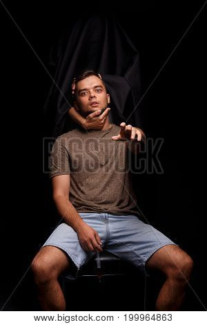 Death holding guy's head on a black background. An addict, narcomaniac with a syringe stretches his hand towards the camera. A young man fighting with drug addiction. Addiction treatment concept.