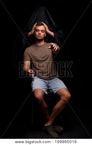 Death holding guy's head on a black background. An addict, narcomaniac with a syringe stretches his hand towards the camera. A young man fighting with drug addiction. Addiction treatment concept.
