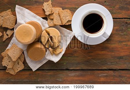 Norwegian homemade brown cheese brunost with crackers and cup of coffee on wooden desk, top view