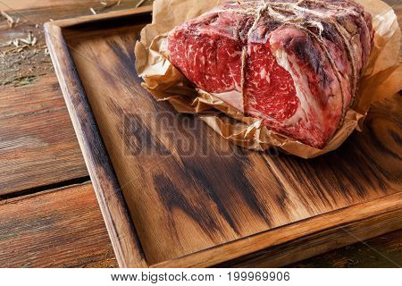 Raw black angus beef bound with rope in craft paper on cutting board. Aged prime marble meat at rustic wood background, closeup, copy space
