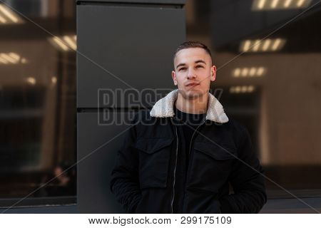 Handsome Attractive Young Man In A Fashionable Black In A Spring Light Jacket Poses Near The Modern