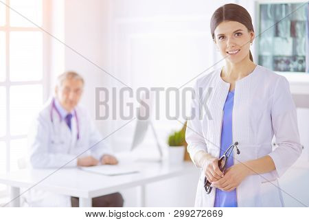 A Doctor Looking At The Camera With Her Male Colleage In The Back Of The Conference Room In Hospital