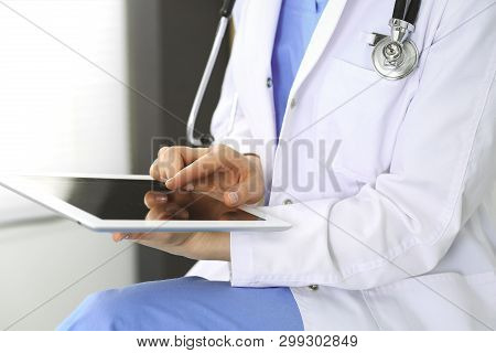 Woman Doctor Using White Tablet Computer While Working In Clinic. Medicine And Health Care Concept