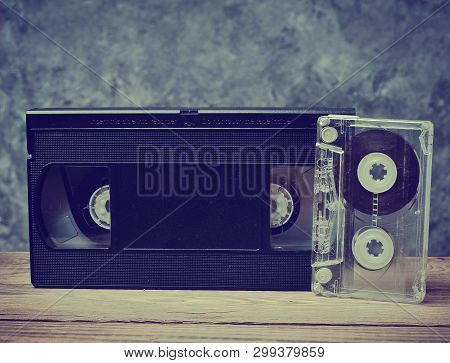 Audio And Video Cassette Close-up On A Wooden Shelf Against A Gray Concrete Wall. Retro Technology F