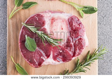 Sliced Meat On A Wooden Board With Herbs And Spices. Raw Meat On The Bone Close-up. Gray Background
