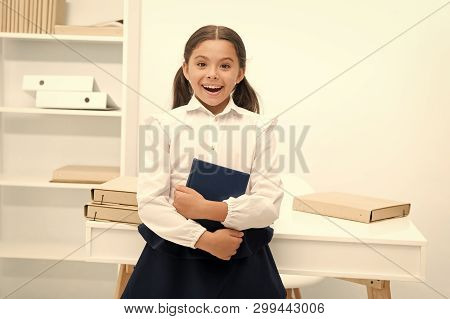 Happy To Enter Into First Form. Girl Child Holds Book Stand Near Table White Background. Schoolgirl 