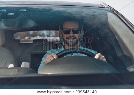 Driving His Brand New Car. Handsome Young Man Smiling While Driving A Status Car