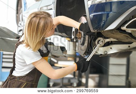 Side View Of Female Mechanic Holding Wrench, Repairing, Fixing Brake Disc Of Automobile Lifted On Br