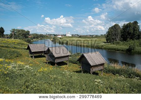 Green Grass And Yellow Wildflowers Grow On The Left Bank Of A Small River And There Are Three Small 