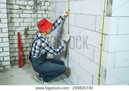 Builder Sitting On His Hunkers Installing Metal Rails Onto Clamps On Block Wall