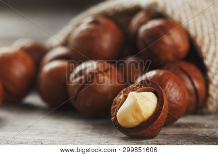 Macadamia Nuts Spilled Out Of The Bag On A Wooden Background Close-up With One Peeled Nut