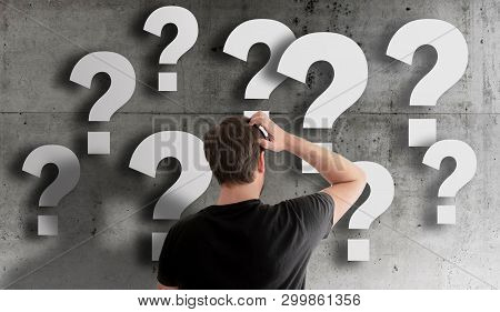 Rear View Of Puzzled Man Scratching His Head Against Concrete Wall Filled With Question Marks