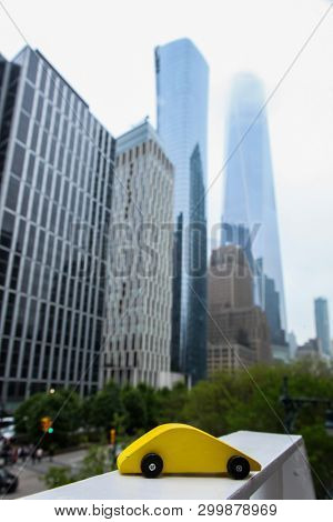 NEW YORK, NY - MAY 03. 2019:  Yellow wooden toy car view from bridge near Borough Of Manhattan Community Colege with One World Trade Center and other buildings.