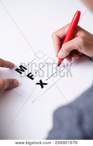 closeup of a young caucasian person about to mark on the X in a form with the letters M for male, F for female and X for the third gender category