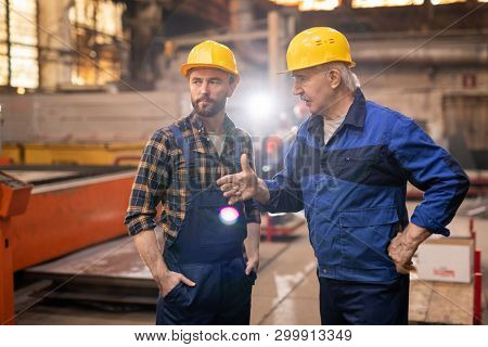 Senior engineer or foreman explaining his trainee how to use new industrial equipment during working day