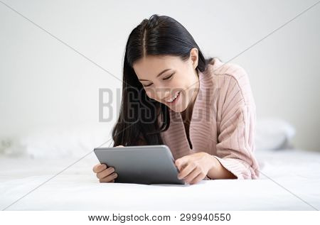 Happy Young Woman Lying On The Bed With Tablet And Surfing Internet At Home Bedroom.technology, Inte