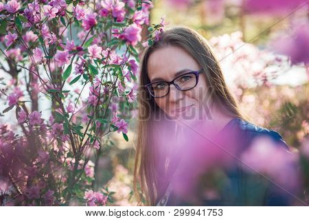 Portrait of young beauty woman in purple rhododendron flowers. Blooming rhododendron - maralnik in Altai mountain forest in the spring.