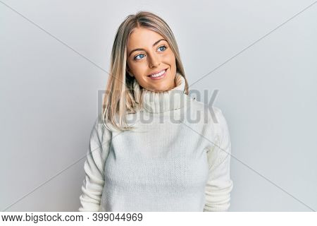 Beautiful blonde woman wearing casual turtleneck sweater looking to side, relax profile pose with natural face and confident smile. 